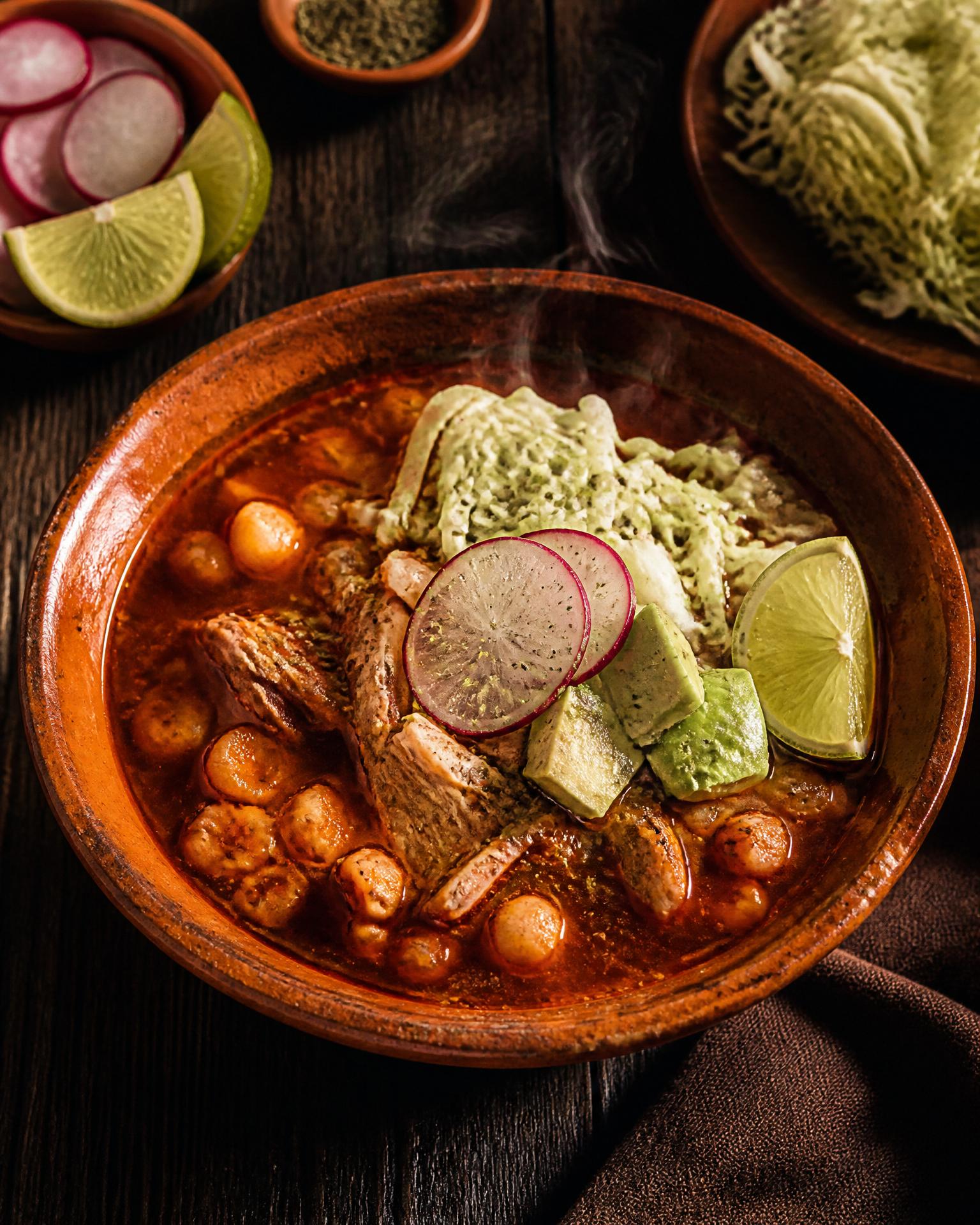 Overhead shot of pozole rojo in a clay bowl with radish and lime